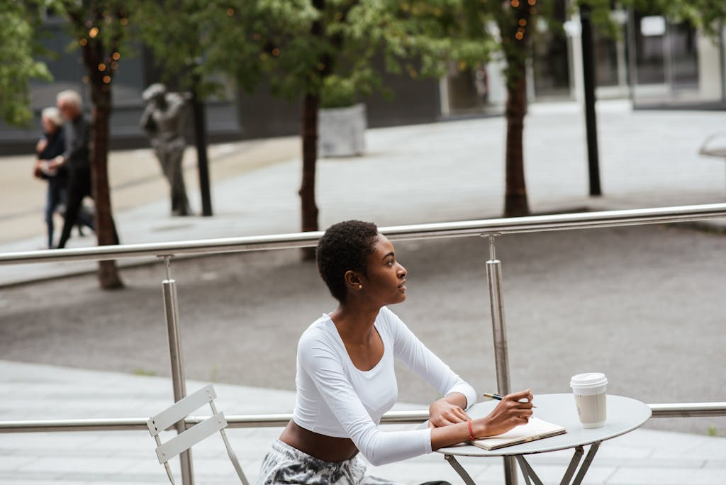 Woman enjoys coffee and notepad outdoors on urban terrace, relaxing and contemplating.