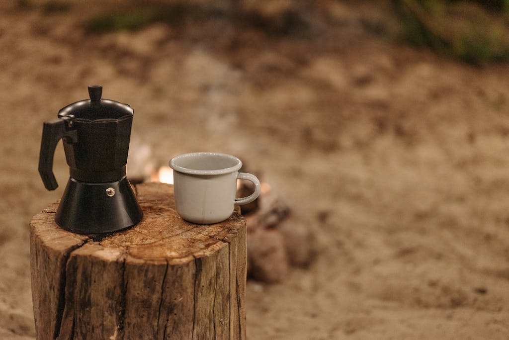 A moka pot and ceramic cup placed on a tree stump outdoors, perfect for a cozy coffee moment.