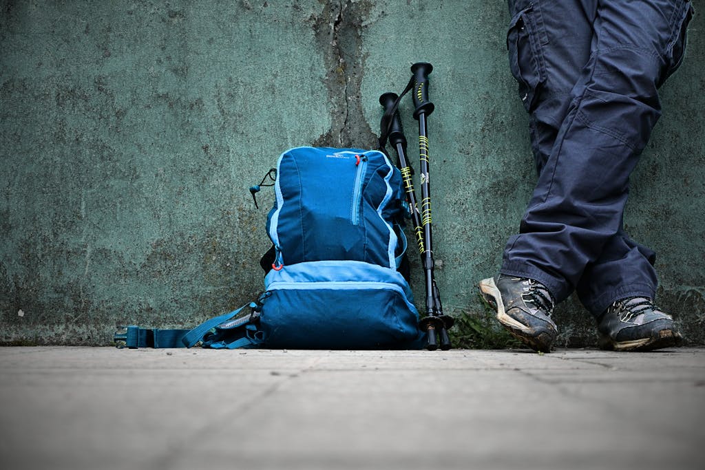 Blue backpack leaning on a wall with hiking poles and gear in an urban setting.
